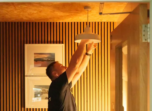 Elektriker monterer en taklampe i et rom med trespiler på veggen